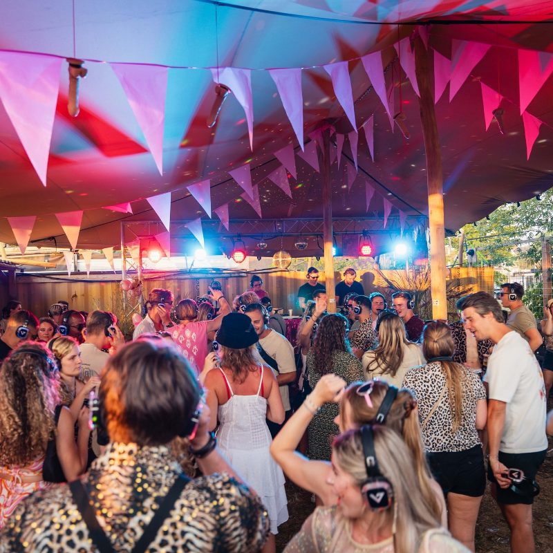 Dansende gasten met silent disco koptelefoons in een versierde feesttent